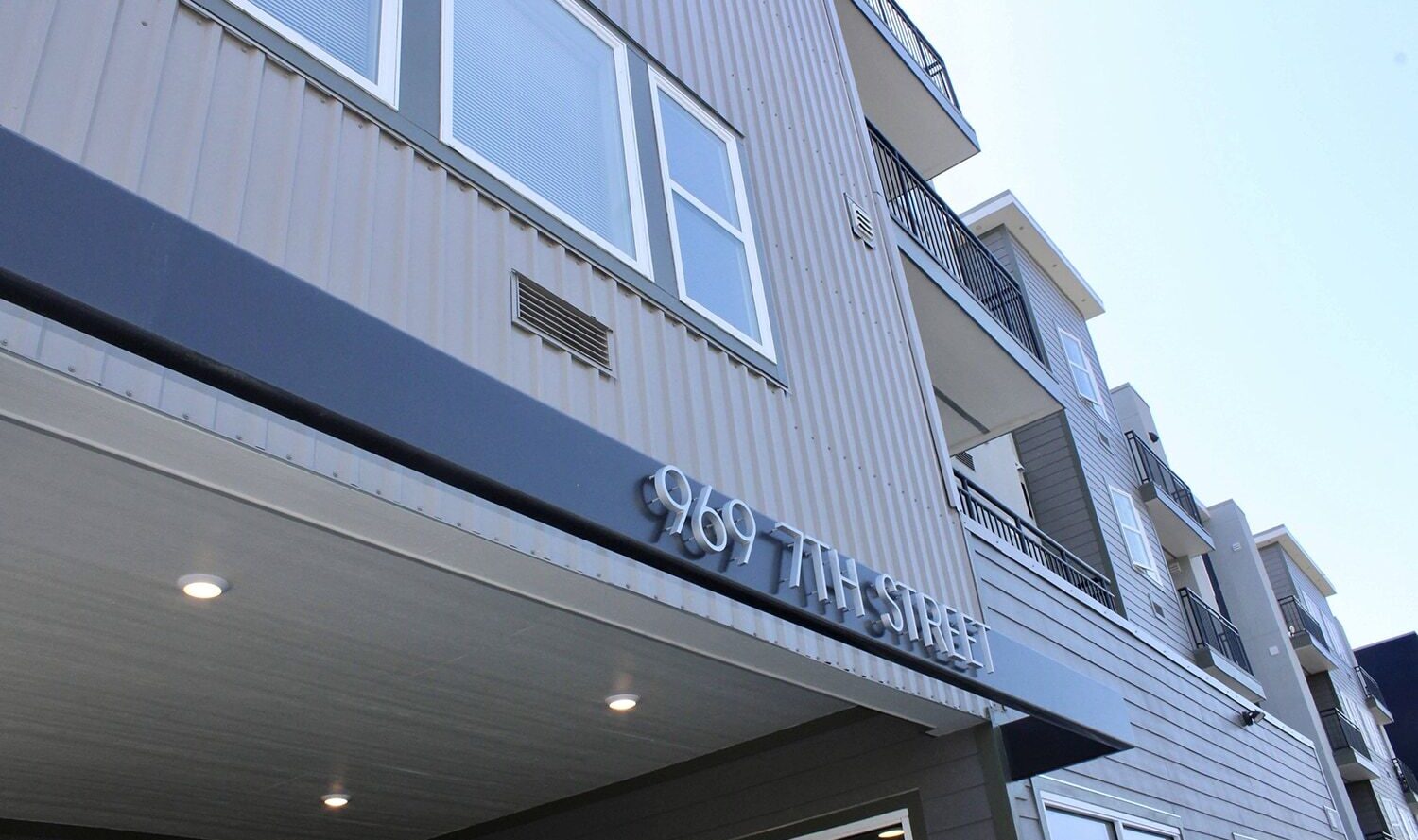 Exterior view of a multi-story building with balconies and large windows. The address 969 7th Street is displayed prominently above the entrance.