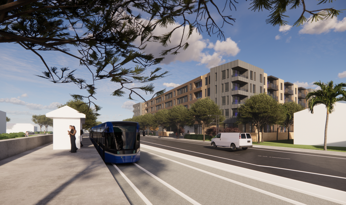 A modern street with a blue tram on the tracks alongside a paved walkway. Two people stand near a tram stop beneath leafy branches. A white van drives on the road. Residential buildings and palm trees line the street under a blue sky with clouds.
