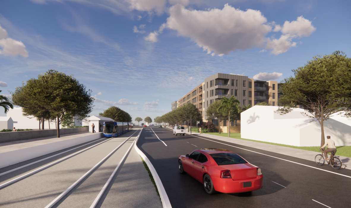 A modern urban street with a red car and a cyclist on the road. Tram tracks run parallel. Tall buildings are on one side, and there are trees lining both sides of the street under a partly cloudy sky.
