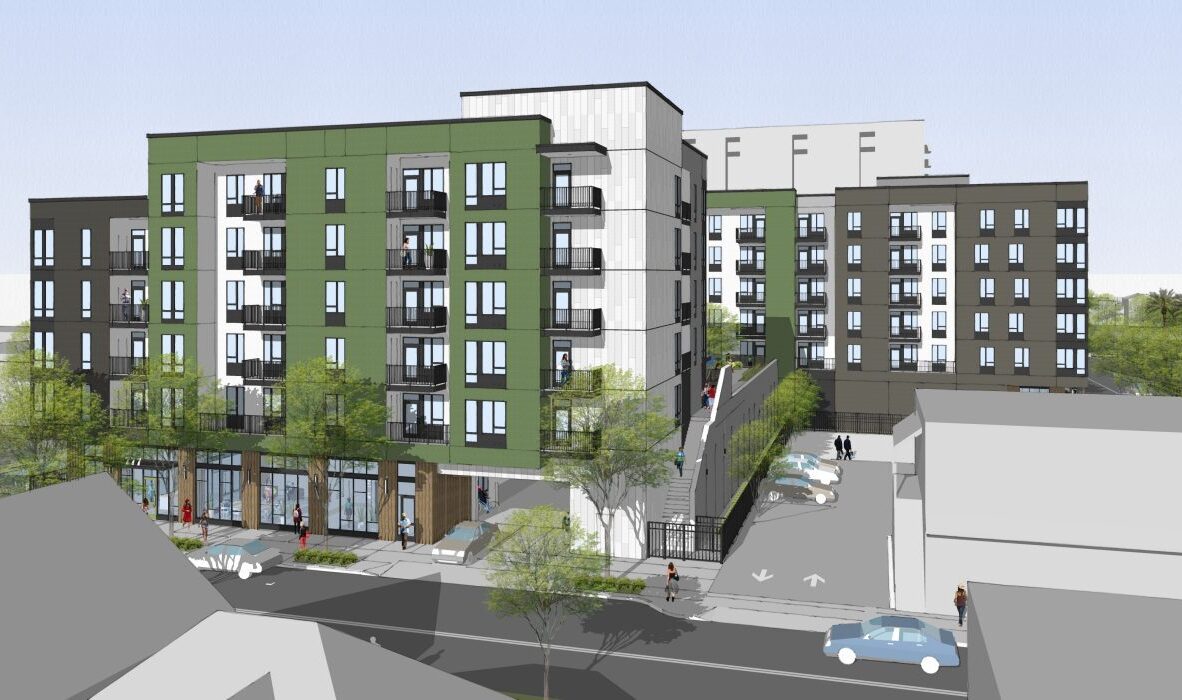 A modern apartment complex with green and white exteriors. The multi-story buildings feature balconies and large windows. Trees line the sidewalks, and there are parked cars and a sloped driveway leading to the entrance.