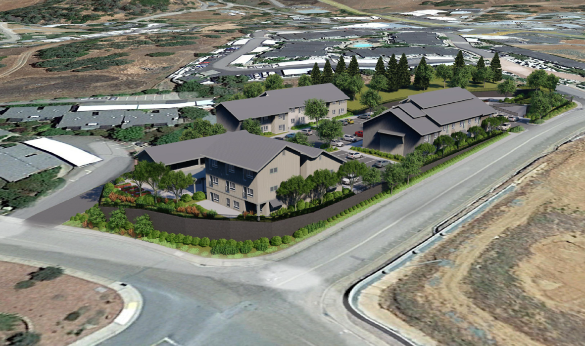 Aerial view of a residential area with several modern houses surrounded by trees and gardens. The neighborhood is bordered by roads and other residential buildings, set in a hilly landscape.