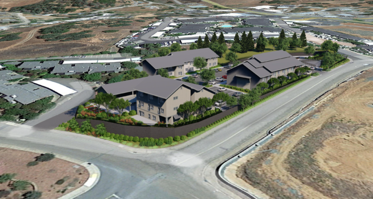 Aerial view of a residential complex with several two-story buildings surrounded by trees and landscaping, located at a road intersection. The complex is situated near open land and other residential areas.